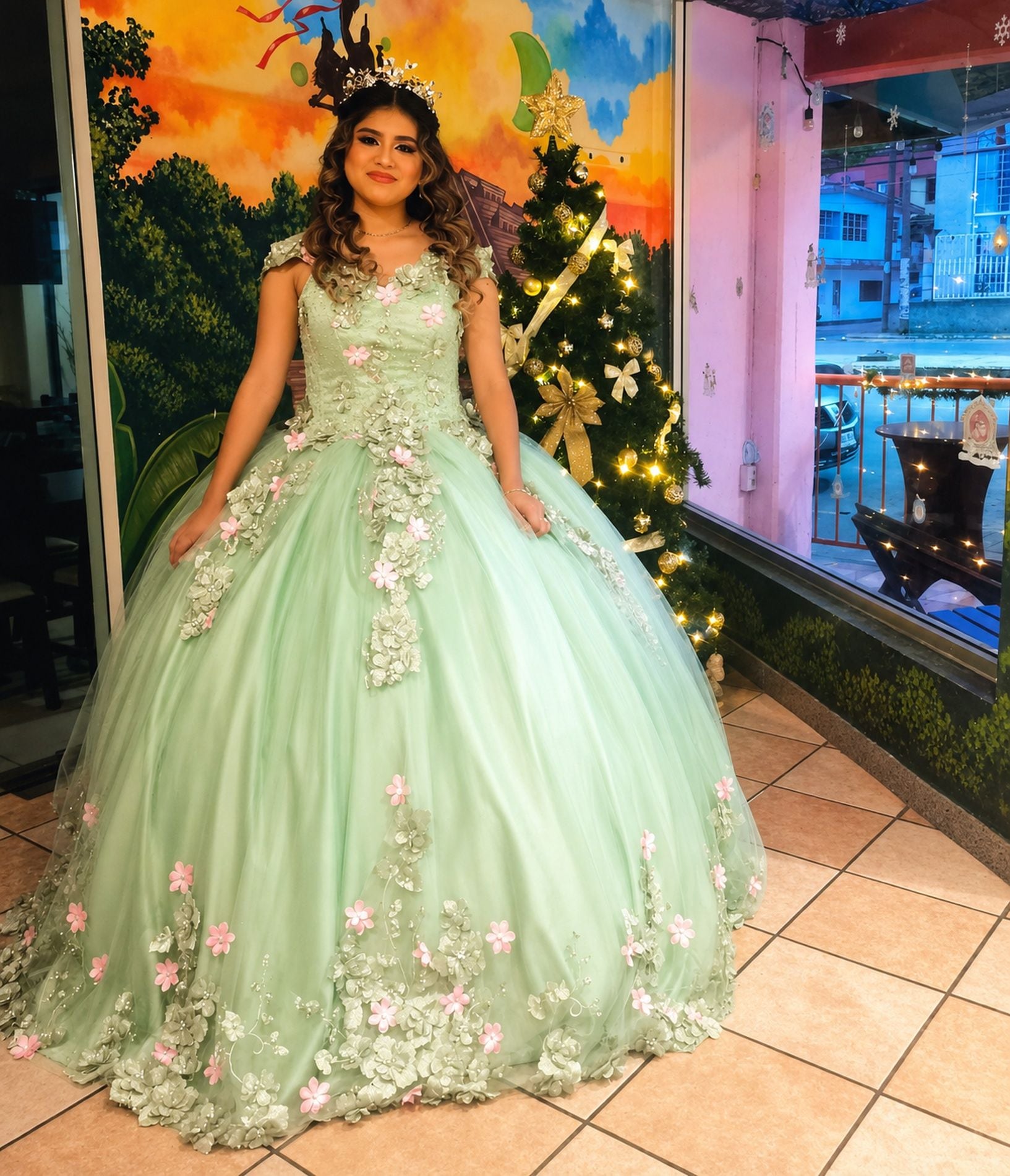 A person in a light green dress with floral embroidery, standing in front of a decorated Christmas tree.