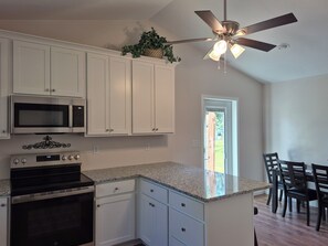 A kitchen with white cabinets, a microwave, an oven, a granite countertop, and a ceiling fan.