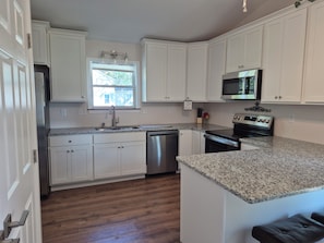 A kitchen with white cabinets, a stainless steel refrigerator, a dishwasher, a microwave, and a granite countertop.