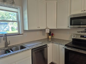A kitchen with white cabinets, a stainless steel sink, a dishwasher, a microwave, and a stove.
