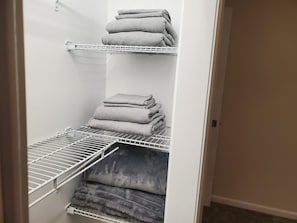 A storage closet with metal shelves holding folded towels.