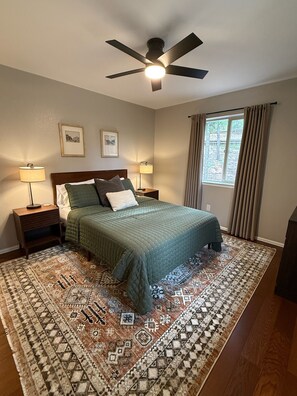 A bedroom with a bed, two bedside tables, a ceiling fan, a window with curtains, and a patterned rug. - Summitview Chalet - Mountain Views & CO Charm (Woodland Park)