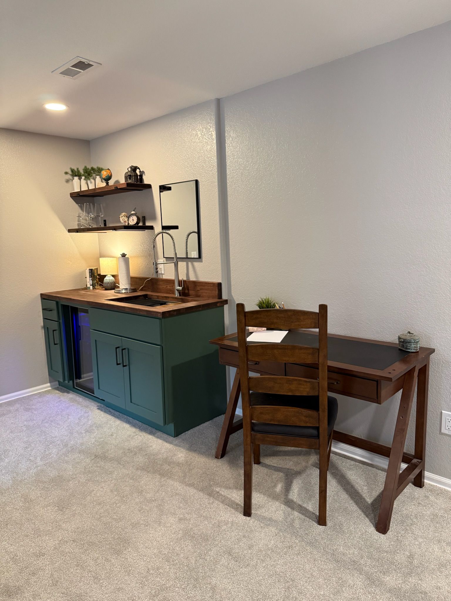 Une cuisine compacte comprenant un évier, un plan de travail et des placards, une table à manger avec une chaise, et une étagère avec des objets décoratifs.