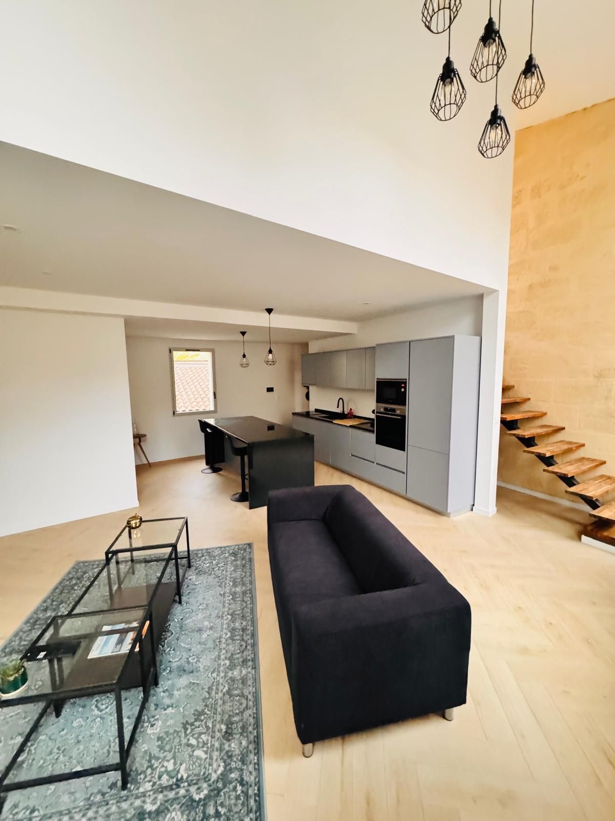 A modern living space with a black sofa, a glass coffee table, and a kitchen area with grey cabinets and a microwave.