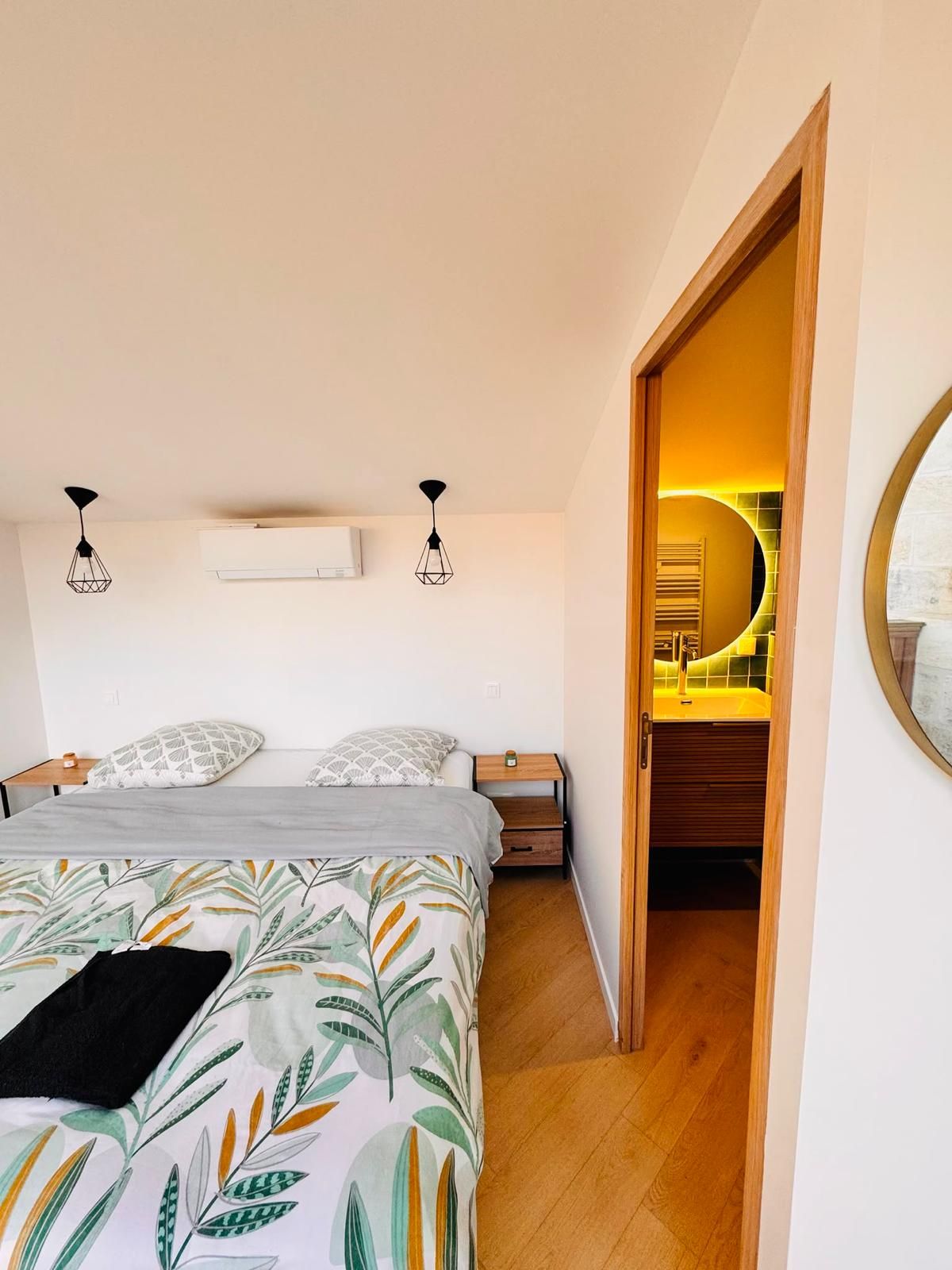 Une chambre à coucher comprenant un lit, des tables de chevet, un appareil de climatisation et donnant sur une salle de bain.