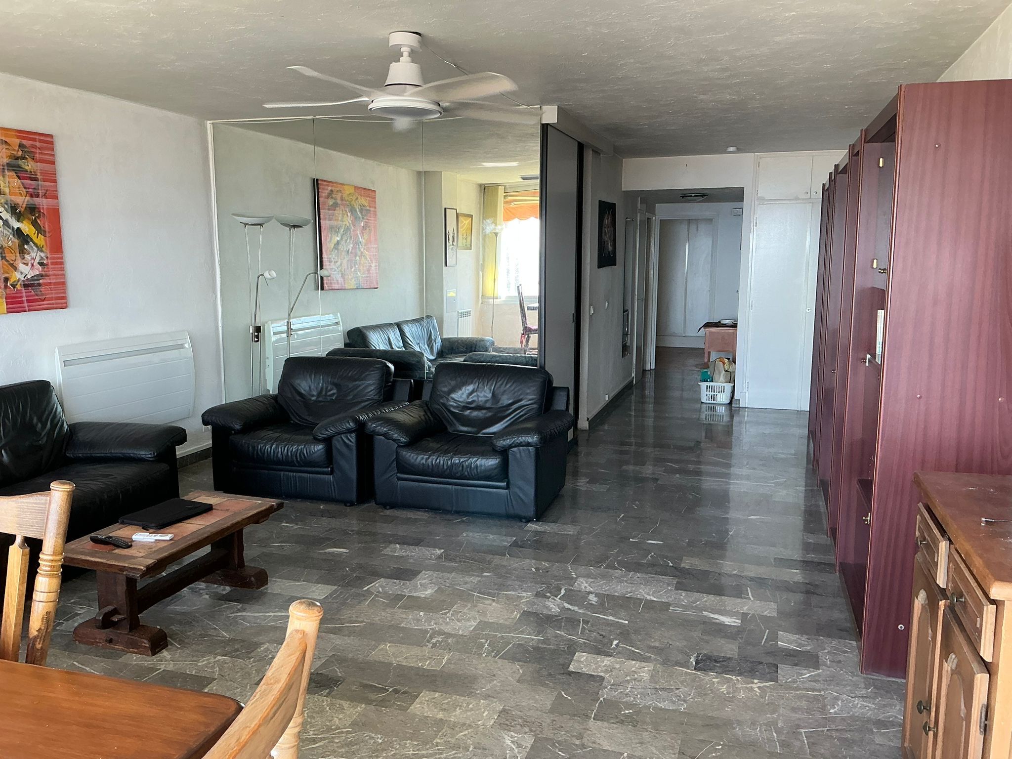 A spacious living area with a black leather sofa set, a wooden coffee table, and a ceiling fan.