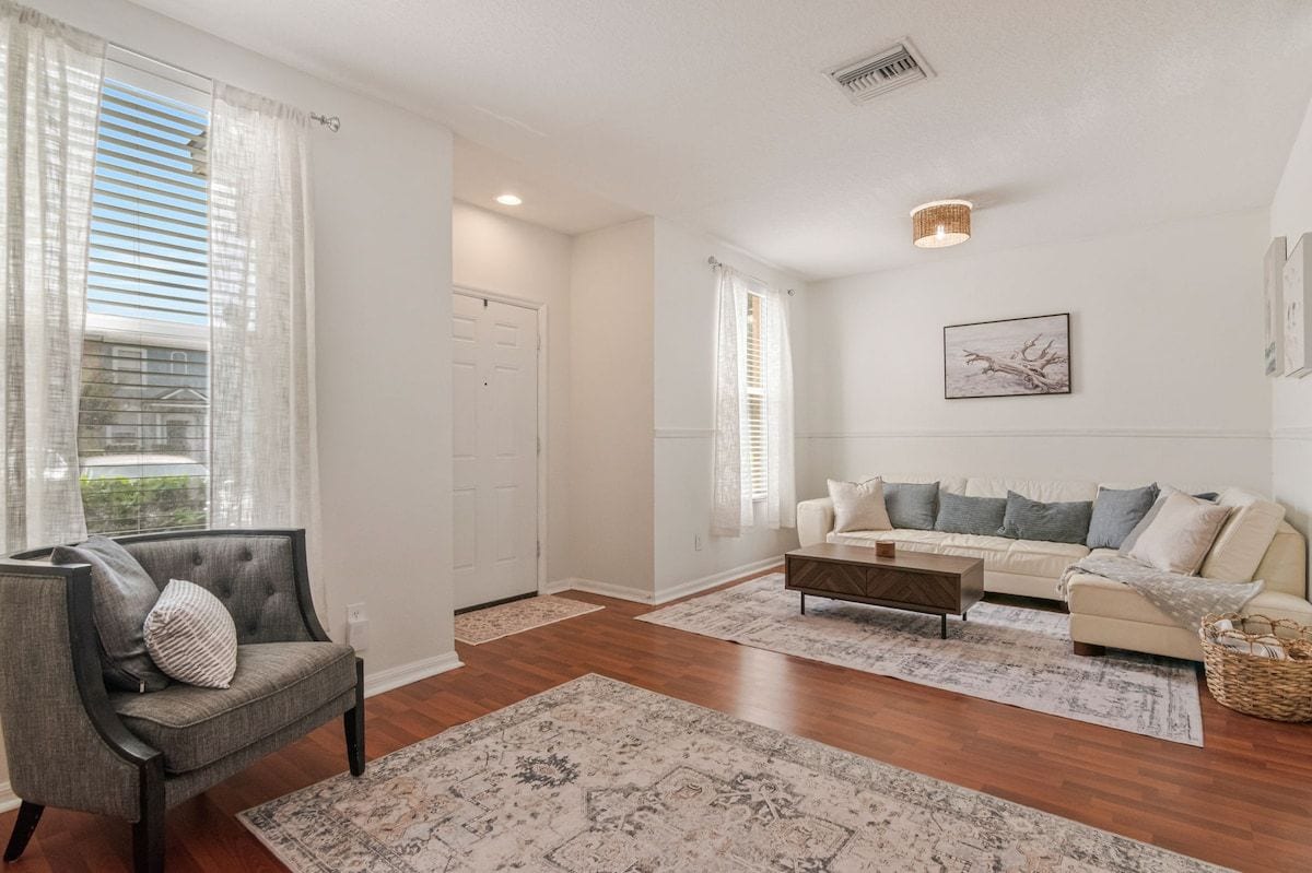 A living room with a sofa, armchair, coffee table, and a large window with curtains.