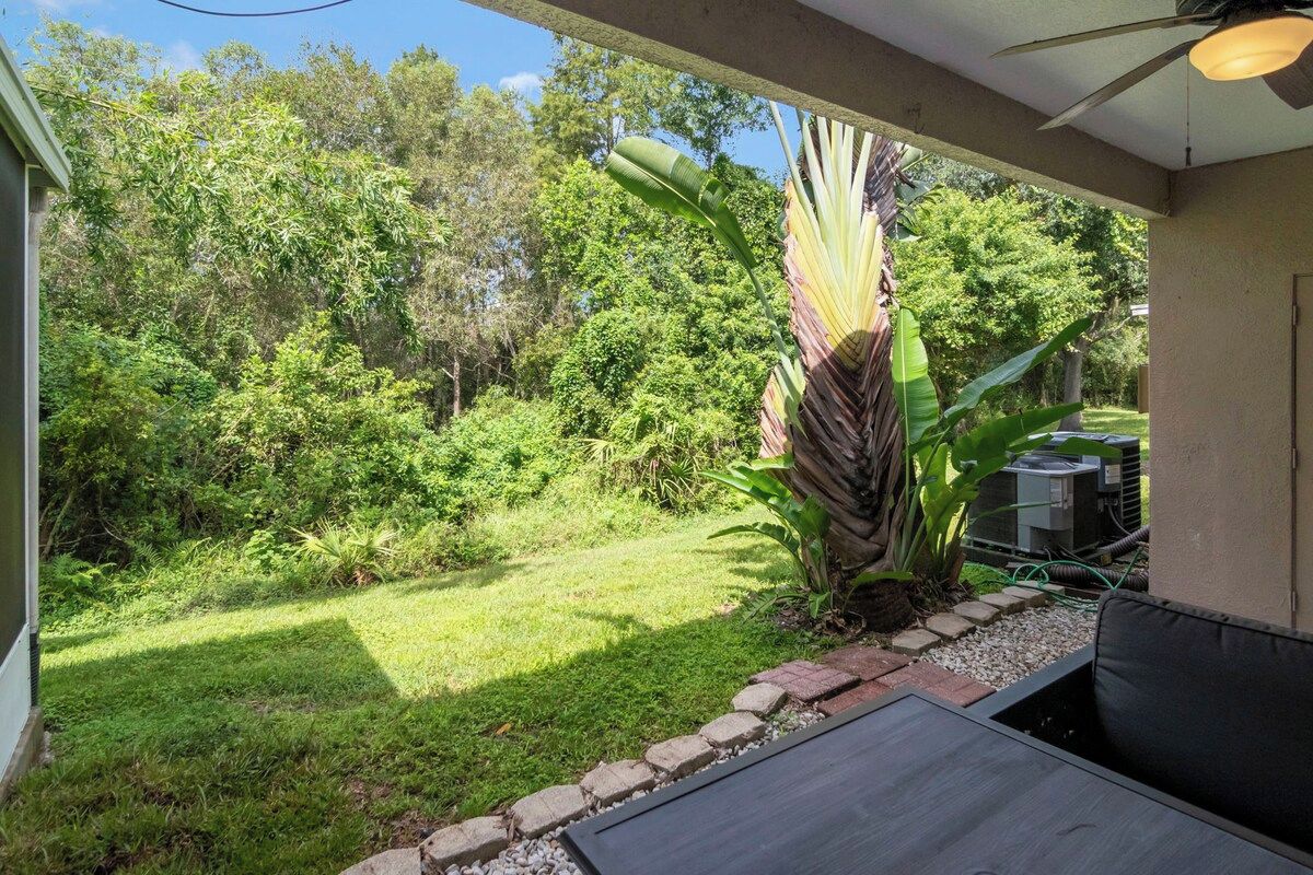 A covered outdoor area with a patio table and chairs, surrounded by lush greenery and a large banana plant.