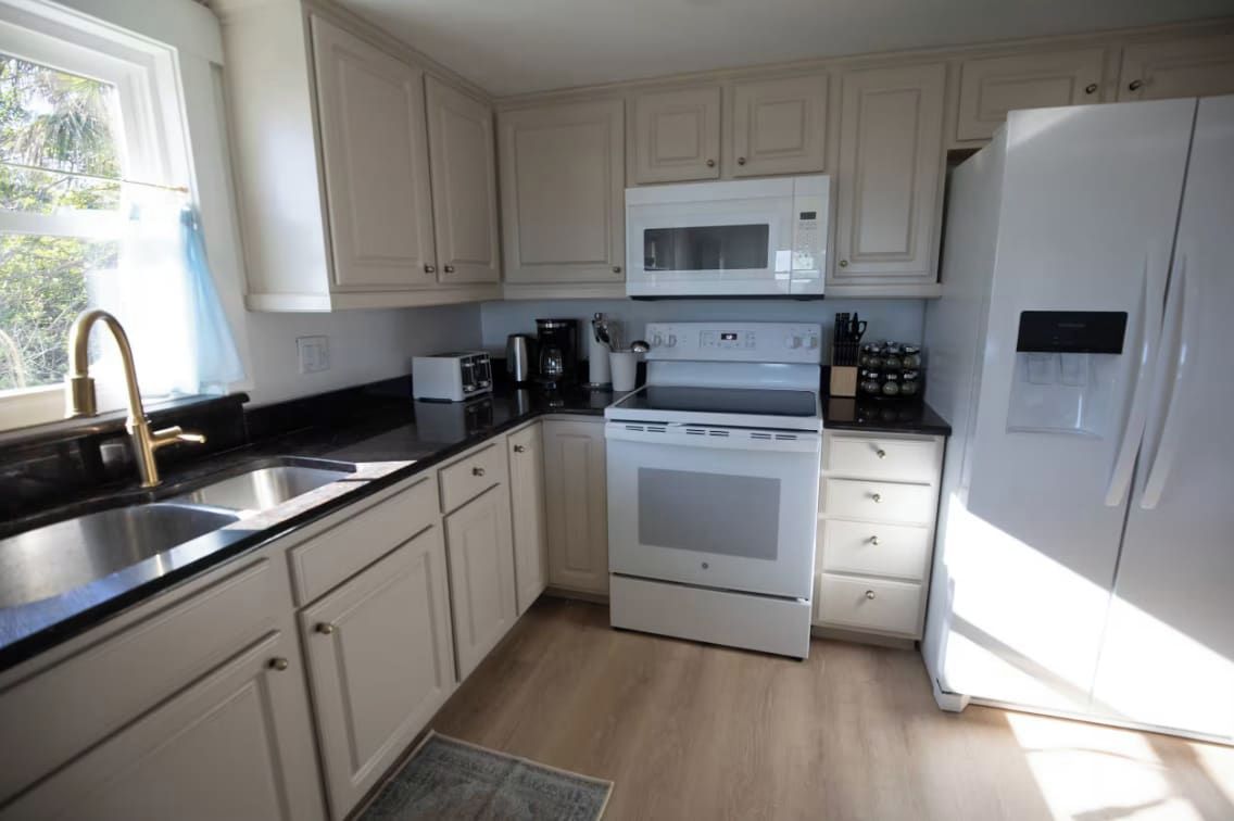 A kitchen with white cabinets, a stainless steel sink, a microwave, a stove, and a refrigerator.