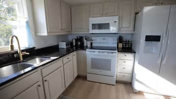 A kitchen with white cabinets, a stainless steel sink, a microwave, a stove, and a refrigerator.