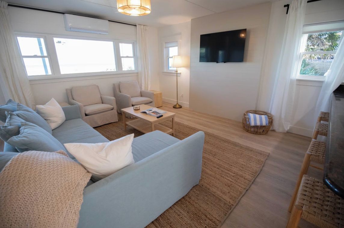 A living room with a sofa, armchairs, a coffee table, a TV, and a window with curtains.