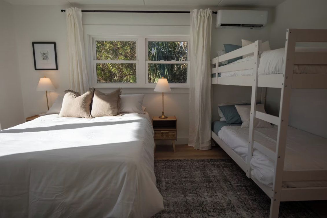 Un dormitorio con una cama individual, una litera, una mesita de noche con lámpara, una ventana con cortinas y un equipo de aire acondicionado.