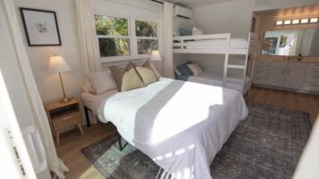 A bedroom with a bed, a bedside table, a lamp, a bunk bed, and a mirror.