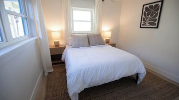 Un dormitorio con cama, dos lámparas de noche, una ventana con cortinas y una obra de arte en la pared.
