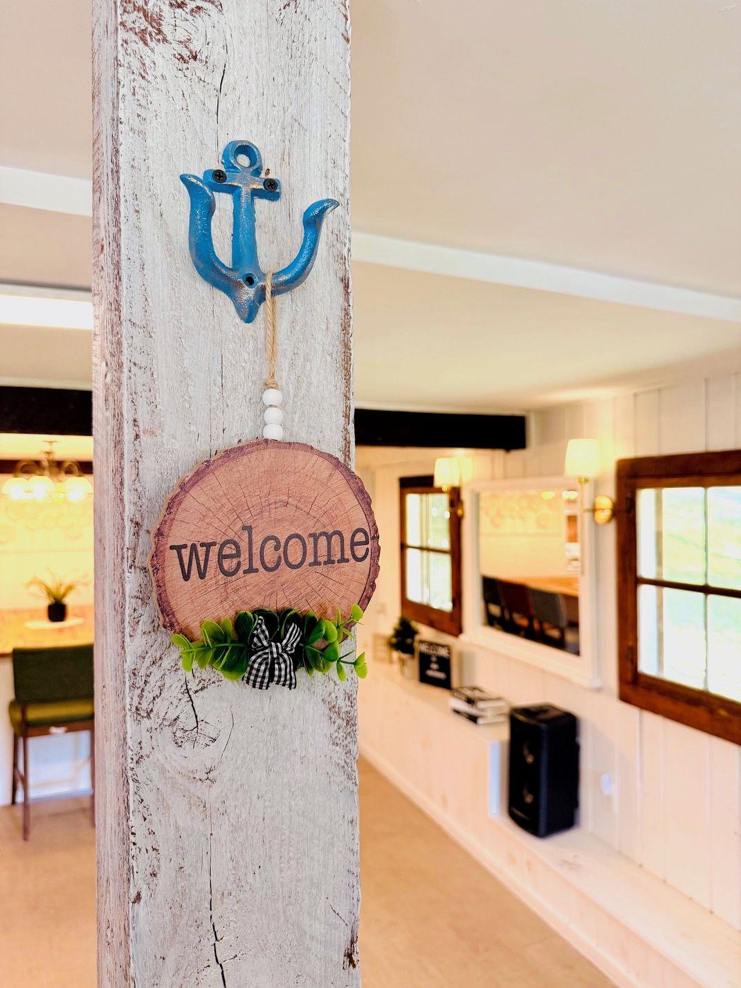 A wooden post with a 'welcome' sign, an anchor decoration, and a small plant.