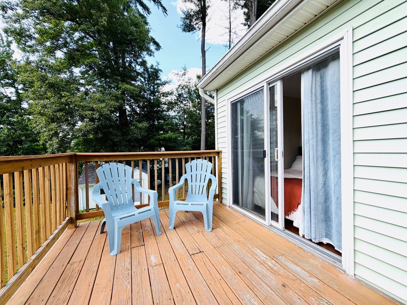 Une terrasse en bois avec deux fauteuils Adirondack et une porte-fenêtre coulissante donnant sur une pièce.