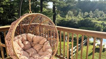 A wicker hanging chair with a cushioned seat on a wooden deck overlooking a forested area.