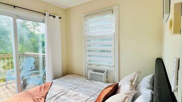 A bedroom with a bed, a ceiling fan, a window with blinds, and a view of the outdoors.