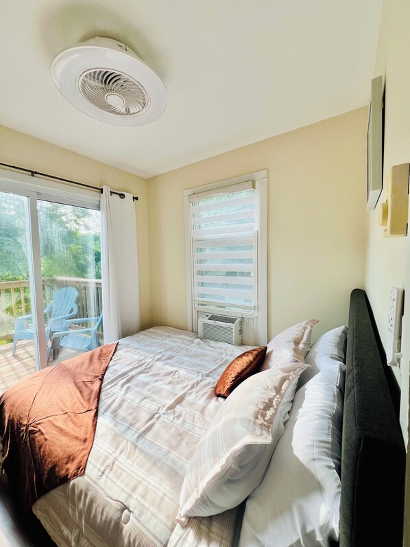 A bedroom with a bed, a ceiling fan, a window with blinds, and a view of the outdoors.