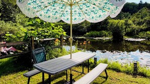 A picnic table with a patterned umbrella, a bench, and a pond in the background.