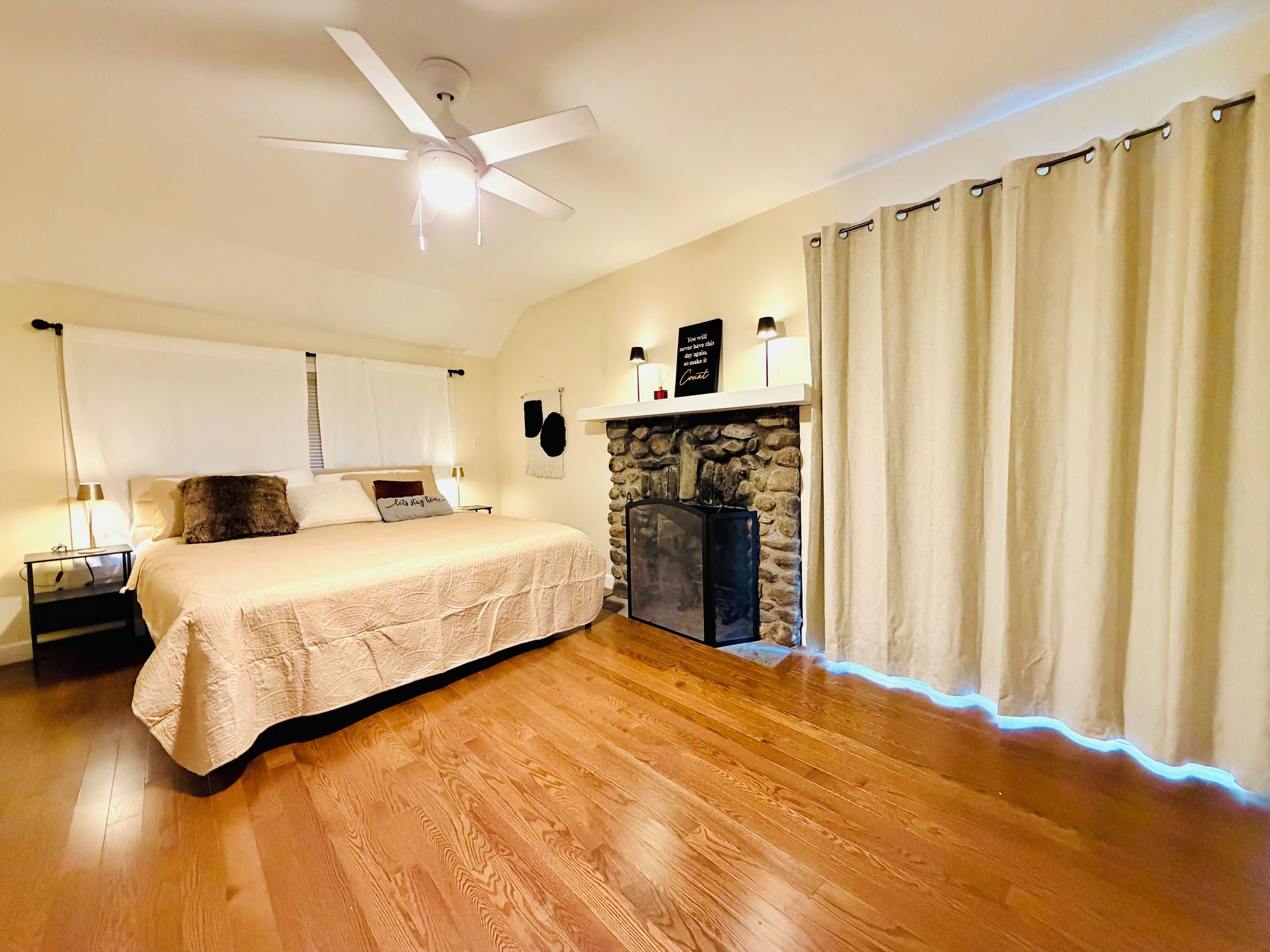 A bedroom with a bed, a ceiling fan, a stone fireplace, and a nightstand.