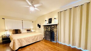 A bedroom with a bed, a ceiling fan, a stone fireplace, and a nightstand.