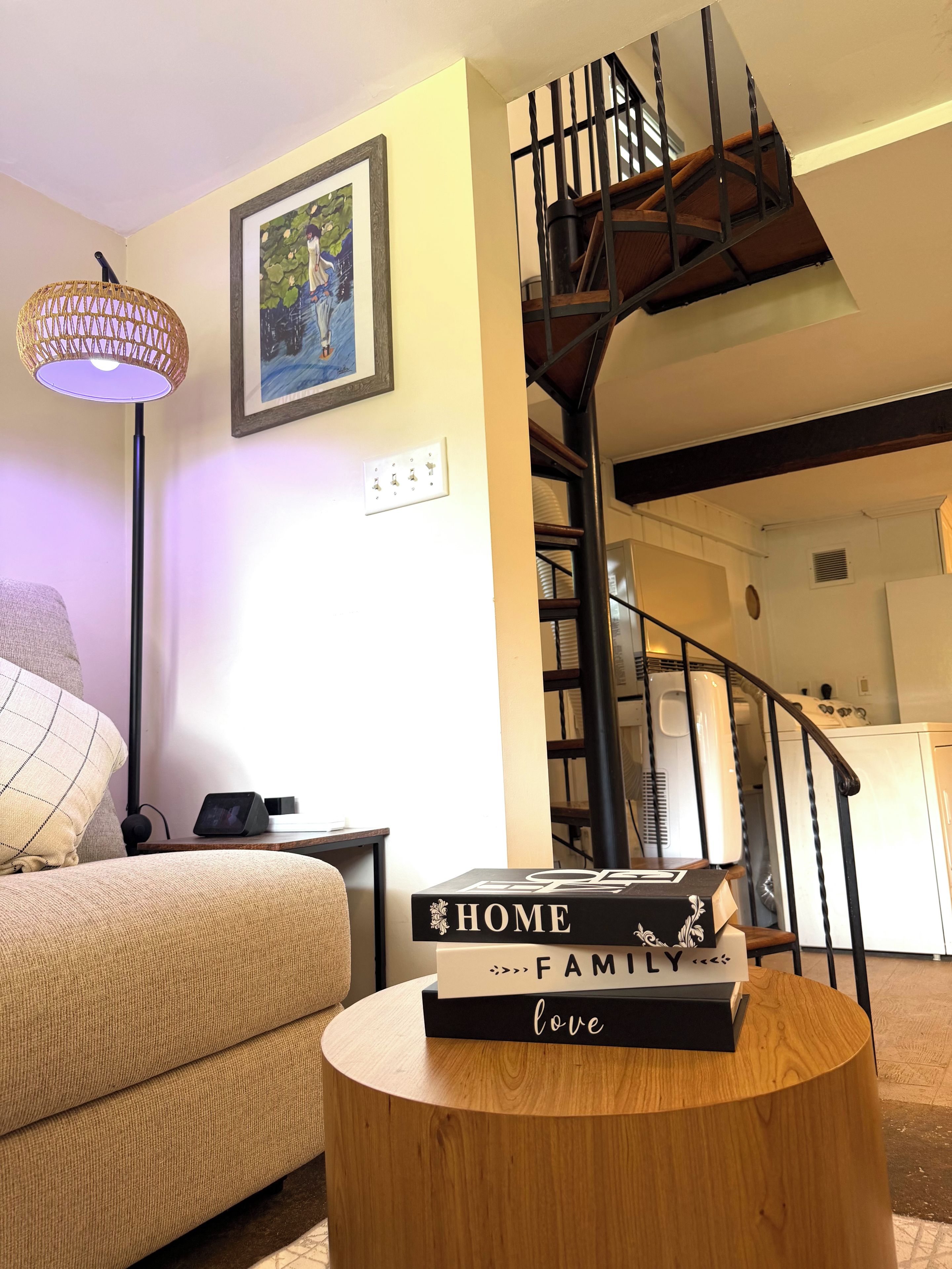 A living room with a sofa, a lamp, a bookshelf, and a staircase.