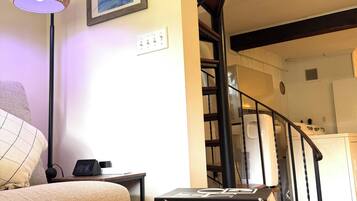 A living room with a sofa, a lamp, a bookshelf, and a staircase.