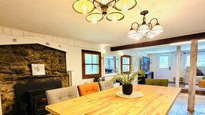 A spacious dining area with a wooden table, chairs, and a potted plant. A stone fireplace and a stone wall are visible in the background.