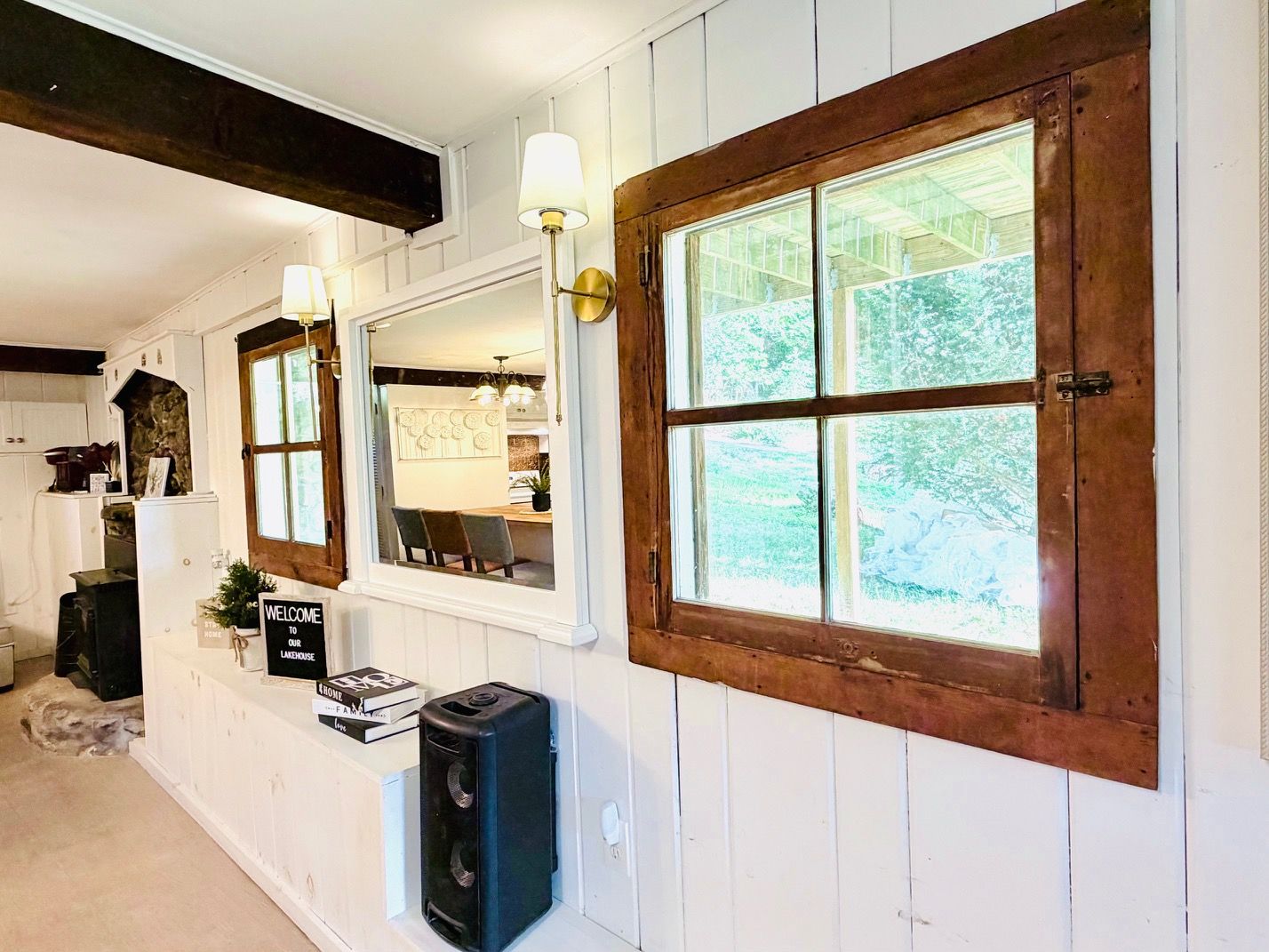 A room with a large window, a wooden door, and a white wall with a welcome sign.