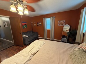 A bedroom with a bed, a gray couch, a ceiling fan, and a window with curtains.
