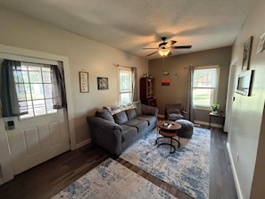 A living room with a gray sofa, a coffee table, a ceiling fan, and a large window with curtains.