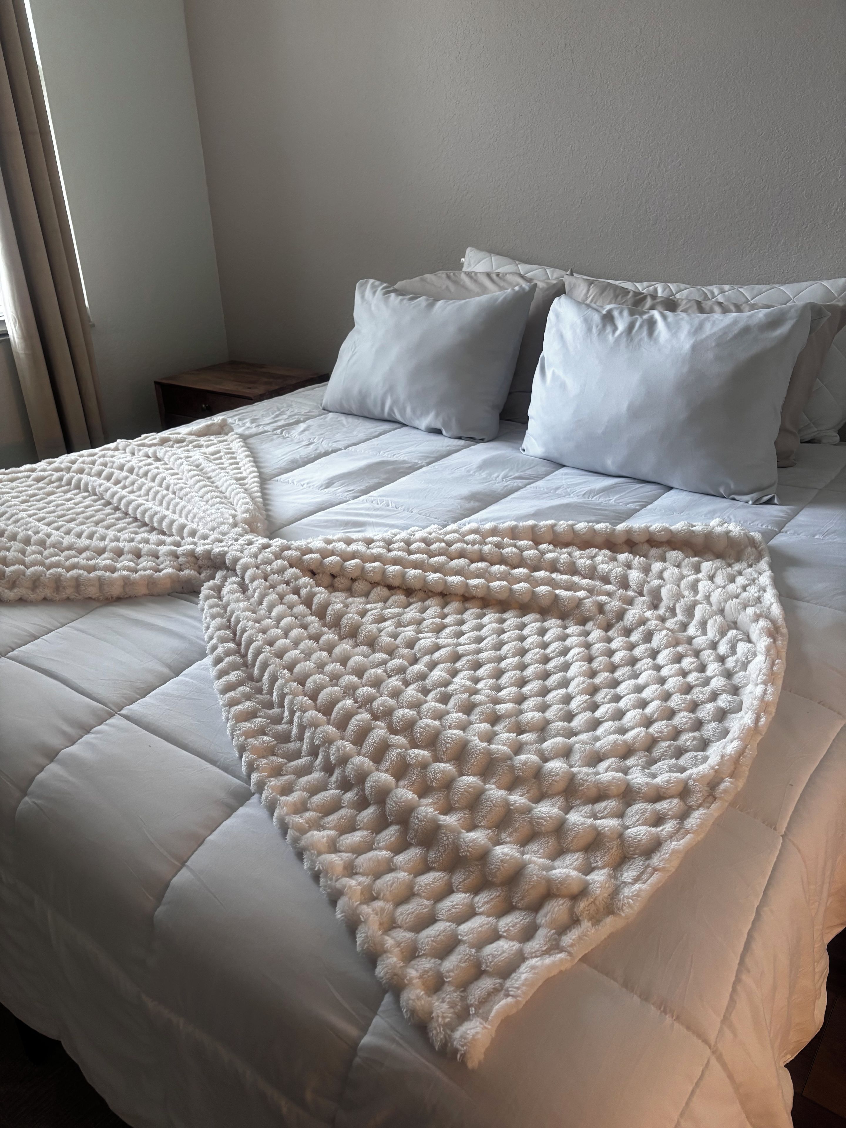 A bed with a white quilt and a large, textured throw blanket.
