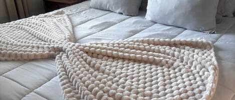A bed with a white quilt and a large, textured throw blanket.
