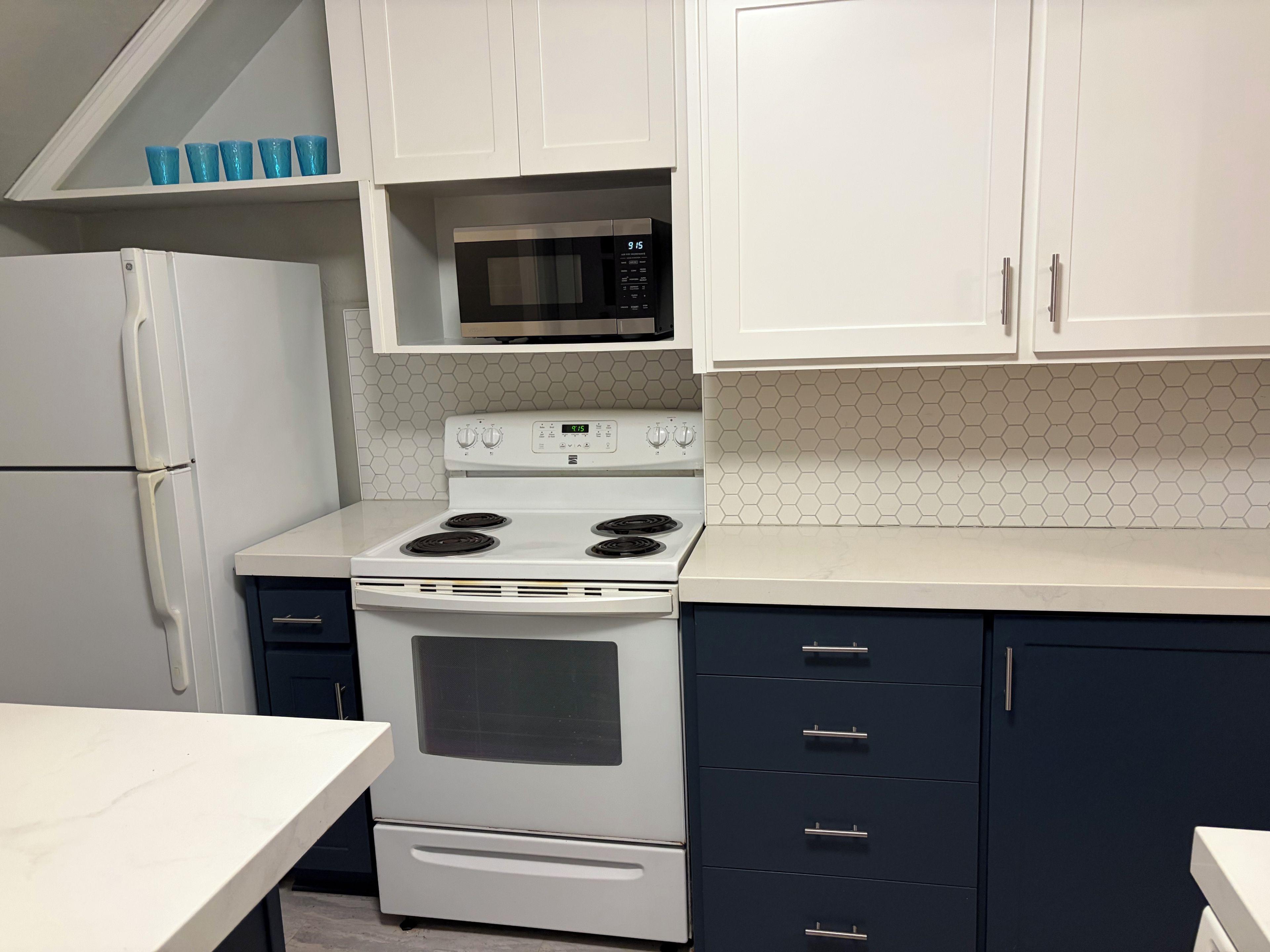 A kitchen with white cabinets, a microwave, a stove, and a refrigerator.