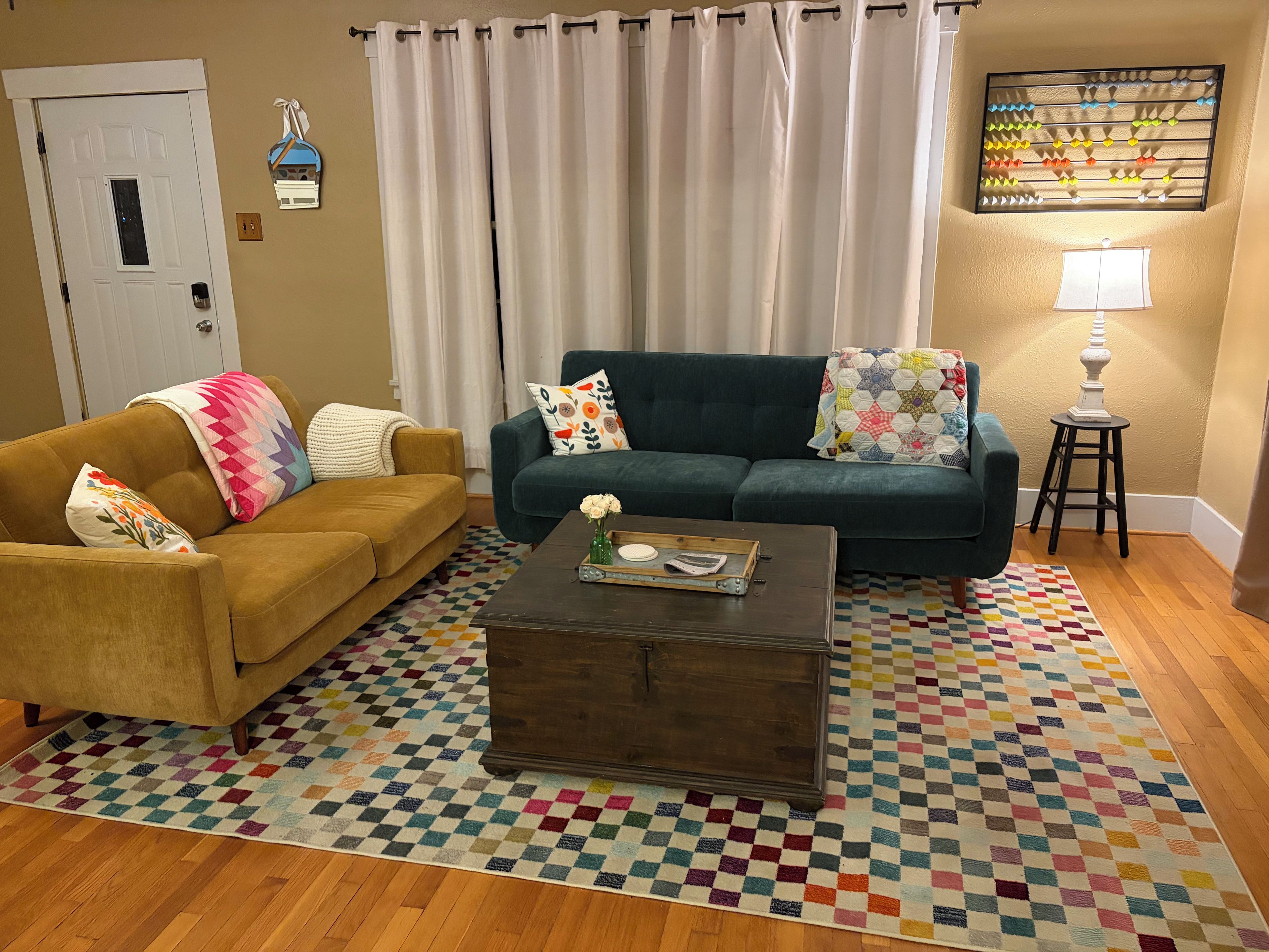 Un salon avec deux canapés, une table basse, un tapis à motifs, une porte et une lampe fixée au mur.
