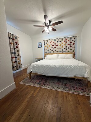 A bedroom with a bed, a ceiling fan, a rug, and curtains.