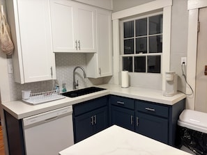 A kitchen with white cabinets, a black sink, a window, and a coffee maker.