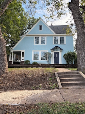 A two-story house with a front porch, a front door, and a small front yard.