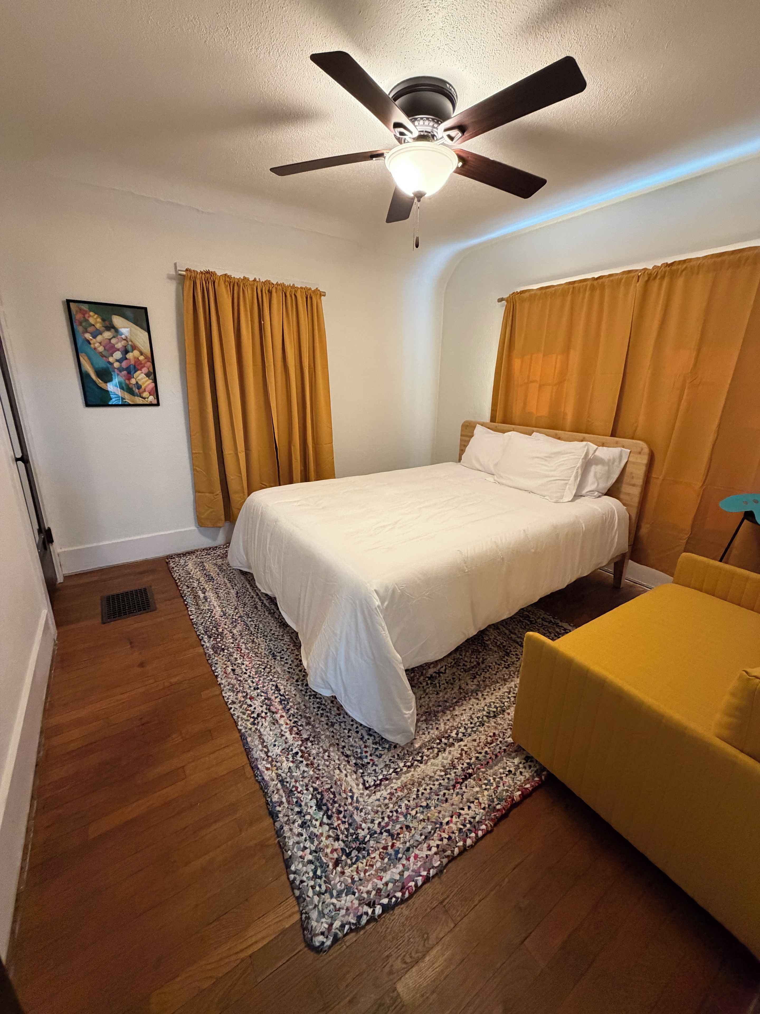 Ein Schlafzimmer mit einem Bett, einem Deckenventilator, einem Teppich und einem gelben Sessel.