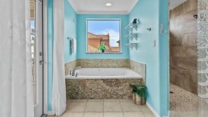 Un baño con una bañera grande, una ventana con vista a una casa y una zona de ducha.