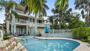 Un edificio de dos pisos con piscina, rodeado de palmeras y un patio amurallado.