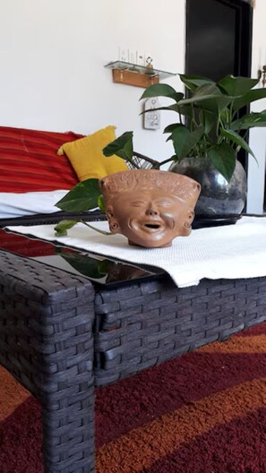 A wicker chair with a white cloth, a potted plant, and a red pillow on a bed.
