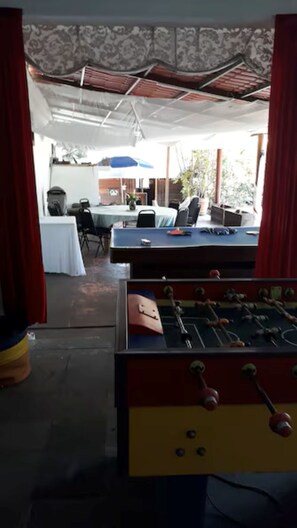 An indoor recreational area with a foosball table, a table tennis table, and a table with chairs.