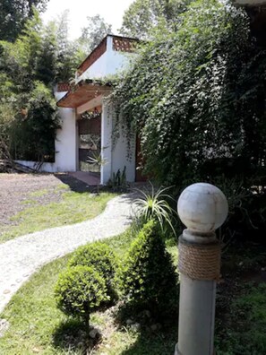 A pathway leading to a building with a white facade and a red roof, surrounded by greenery.