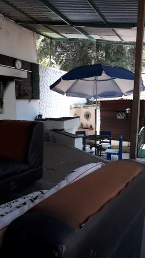 A covered outdoor seating area with a table and chairs, a sofa, and a large umbrella.