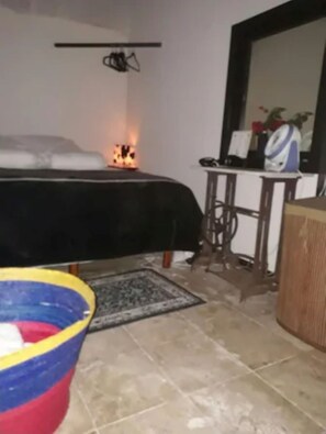 A room with a bed, a small table with a chair, a rug, and a colorful object on the floor.