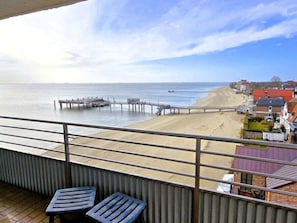 A balcony with two chairs, a view of a beach, a pier, and a row of houses. - Holiday Apartment in Fohr With 1 Bedroom (Wyk auf Foehr)