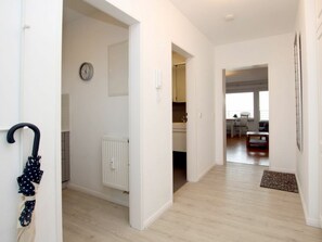 A hallway with a radiator, a clock, and a door leading to a living area with a sofa and a coffee table. - Holiday Apartment in Fohr With 1 Bedroom (Wyk auf Foehr)