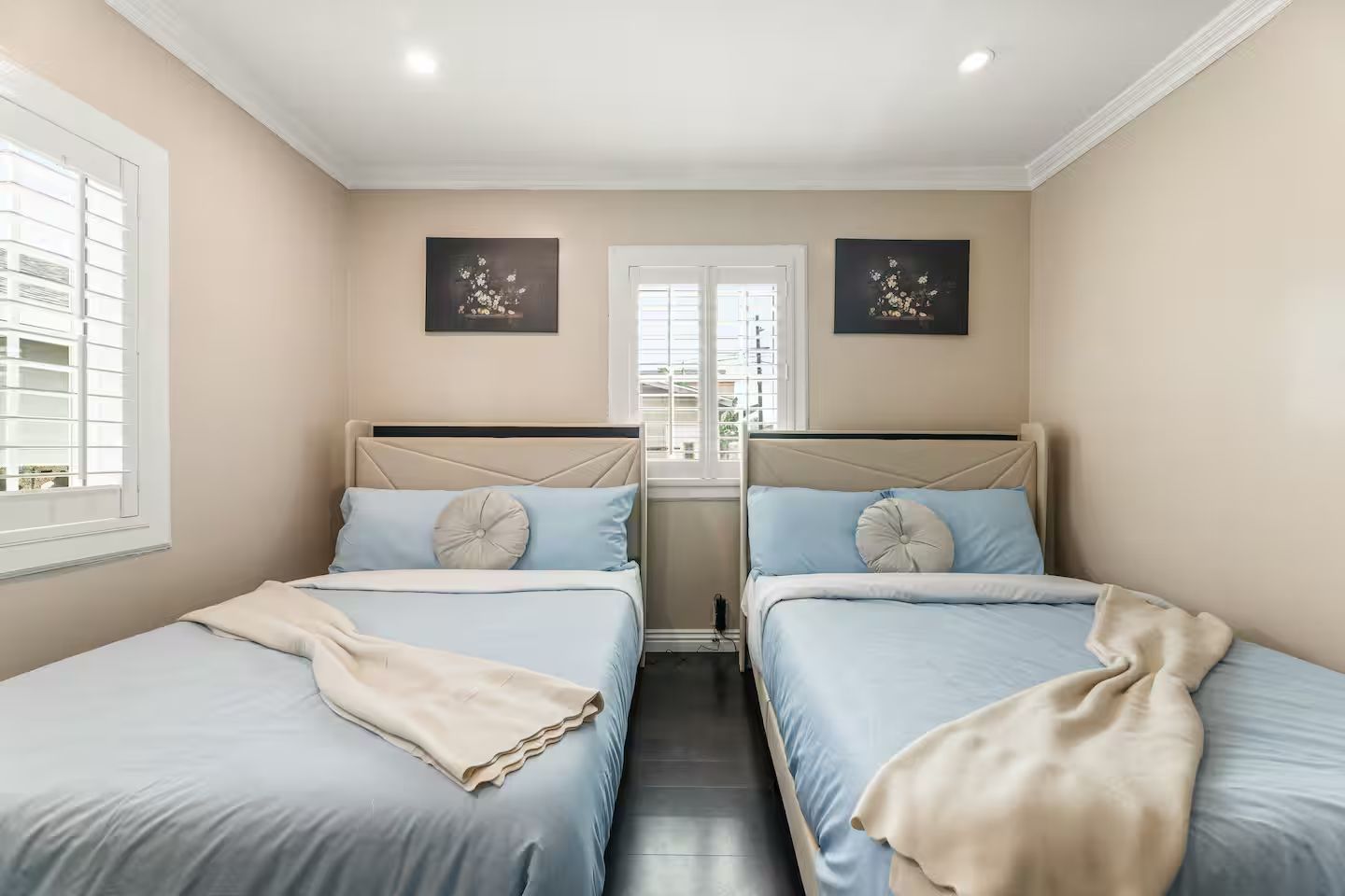 A hotel room with two beds, a window with blinds, and artwork on the walls.
